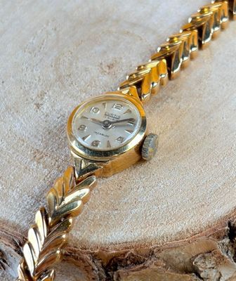 a gold wrist watch sitting on a piece of wood