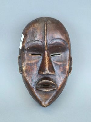 un vieux masque en bois accroché au mur, sur lequel est accrochée une étiquette