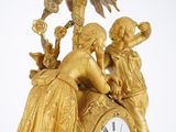 a gold clock with a woman and a man on it