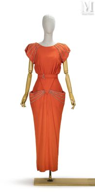 une robe orange posée sur un socle de mannequin, avec un mannequin blanc
