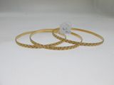 deux bracelets rigides en or posés sur une surface blanche, accompagnés d'une étiquette