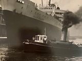 photographie en noir et blanc représentant un remorqueur et un grand navire sur l'eau