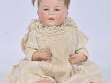 an antique doll sitting on a white surface wearing a white dress