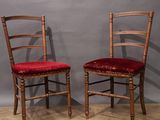 pair of wooden chairs with red upholstered cushions against a gray wall