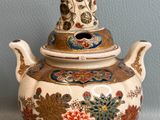 a small teapot with a buddha on top of it