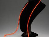an orange beaded necklace on a black mannequin stand