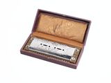 un harmonica argenté dans un étui en bois posé sur une surface blanche