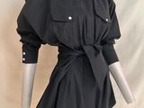 Le mannequin porte une robe-chemise noire avec une ceinture.
