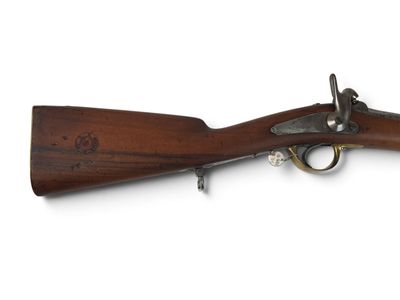 un vieux fusil avec un canon en bois et des accessoires en laiton sur fond blanc