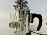 a silver coffee maker with a glass in front of it