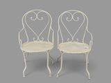 pair of white wrought garden chairs on grey background
