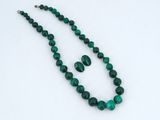 a close up of a green necklace and earrings on a white surface