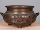 un vieux bol en bronze orné d'un motif de dragon, posé sur une table en bois