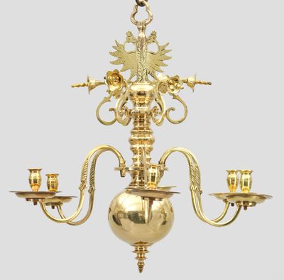 un lustre ancien en laiton, muni de trois bougies et surmonté d'un oiseau