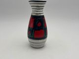 petit vase rouge et noir posé sur une table blanche, sur fond gris