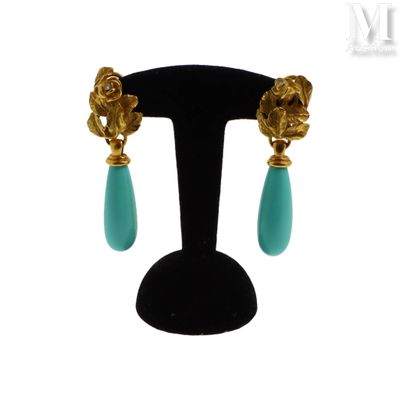 une paire de boucles d'oreilles turquoise et or posées sur un présentoir noir