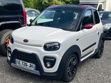 La petite voiture blanche est garée sur le parking, à côté d'autres voitures.