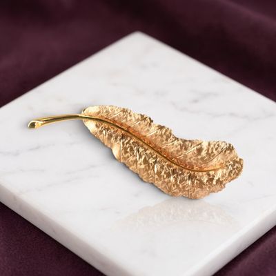 broche en forme de feuille plaquée or posée sur une surface en marbre