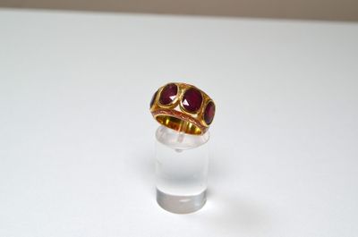 a gold ring with a red stone on top of a clear glass
