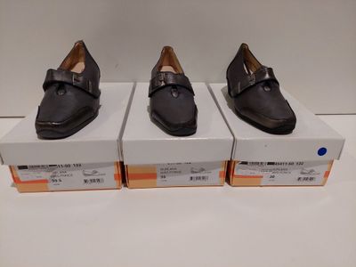 trois paires de chaussures noires posées sur des cartons, sur une surface blanche