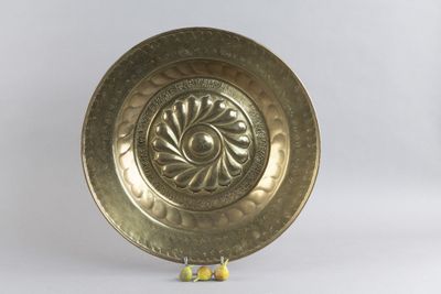 une assiette en or posée sur un socle, sur fond blanc