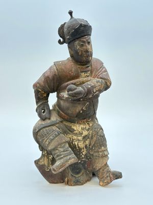 une vieille figurine représentant un homme assis sur un rocher, tenant un poisson