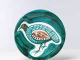 assiette en verre vert sur laquelle est représenté un oiseau, posée sur une surface blanche