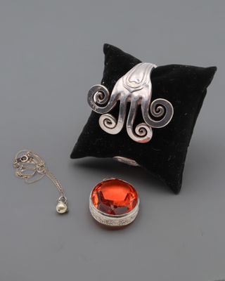 une photo d'une bague en argent sertie d'une pierre orange, posée sur un coussin