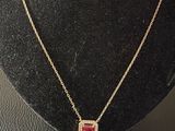 a gold necklace with a red stone on a black mannequin