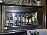 bottles of wine are lined up behind a wine cooler in a bar
