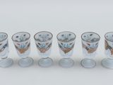 six shot glasses are lined up in a row on a white surface