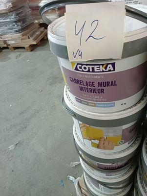 Plusieurs seaux de peinture sont empilés les uns sur les autres dans un entrepôt