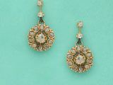 une paire de boucles d'oreilles dorées ornées de pierres blanches sur fond turquoise