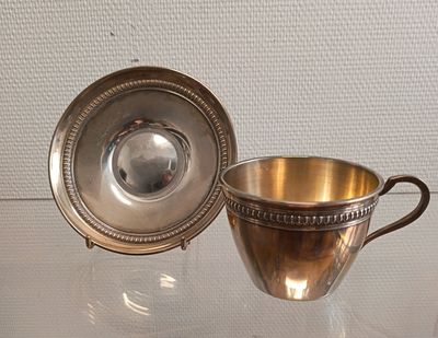 une tasse et une soucoupe en argent posées sur une table en verre