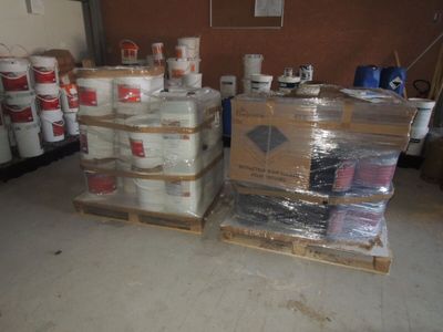 Des cartons de peinture sont empilés sur des palettes dans un garage