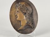 a bronze plate with a woman ' s head and a bird on it