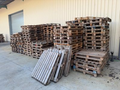 Plusieurs palettes de bois sont empilées devant un bâtiment