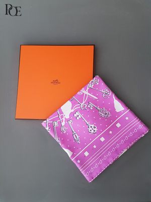 le foulard Hermès et son coffret sont posés sur une surface grise