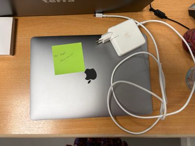 un ordinateur portable Apple sur lequel est collé un post-it, posé sur un bureau