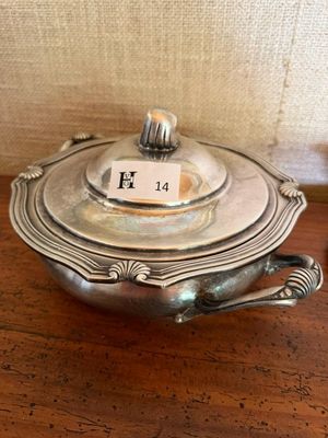 un plat ancien en argent, muni d'un couvercle et d'une poignée, posé sur une table en bois