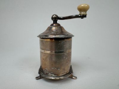 un vieux moulin à café en argent muni d'un manche en bois, posé sur une surface blanche