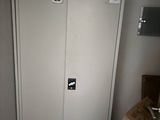 une armoire blanche dans une petite pièce, avec un carton posé par terre