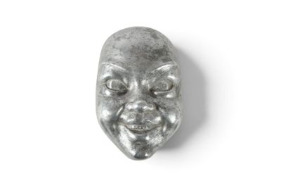 un masque métallique sur lequel est représenté un visage, posé sur une surface blanche