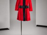 une photo d'un manteau rouge avec une ceinture noire, posé sur un présentoir pour mannequin