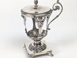 une théière ancienne plaquée argent, posée sur un support, sur fond blanc