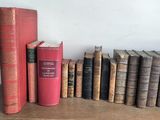 several old books are lined up on a shelf in front of a white wall