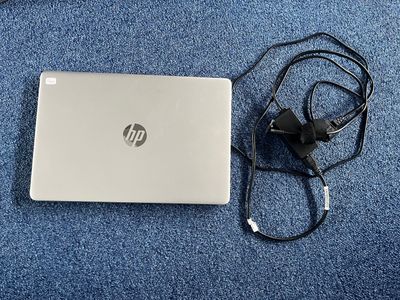 un ordinateur portable posé sur un tapis bleu, avec un chargeur branché dessus