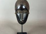 a bronze mask on a black stand with a white background