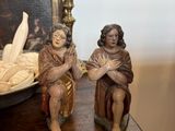 two figurines of people sitting on a table next to a bowl of fruit