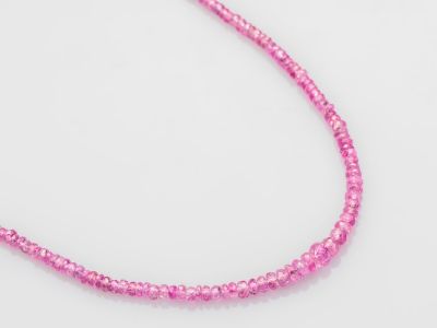 un gros plan d'un collier de perles roses posé sur une surface blanche
